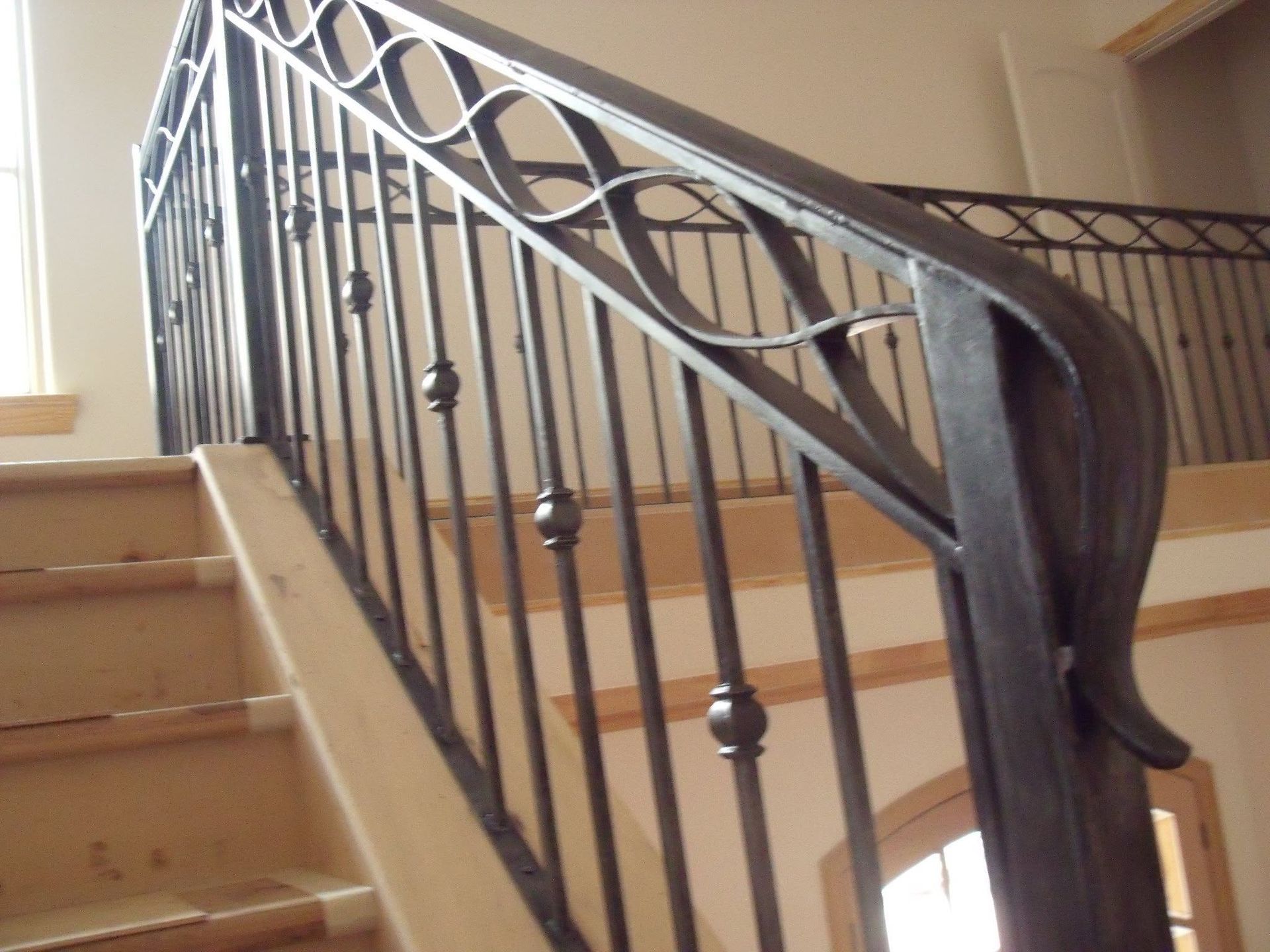 Ornate black metal stair railing beside beige carpeted stairs indoors