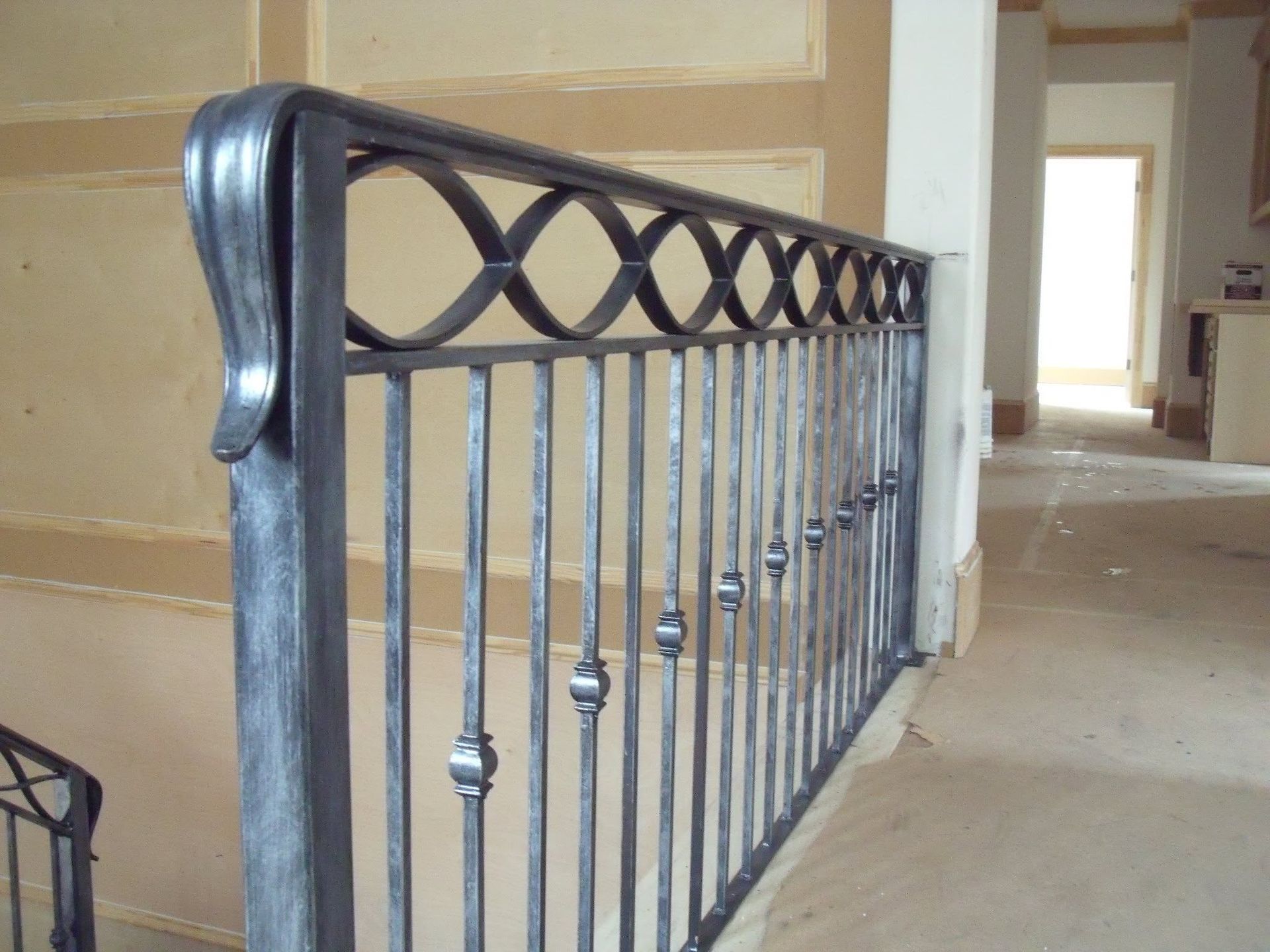 Wrought-iron stair railing with decorative loops in an unfinished indoor hallway