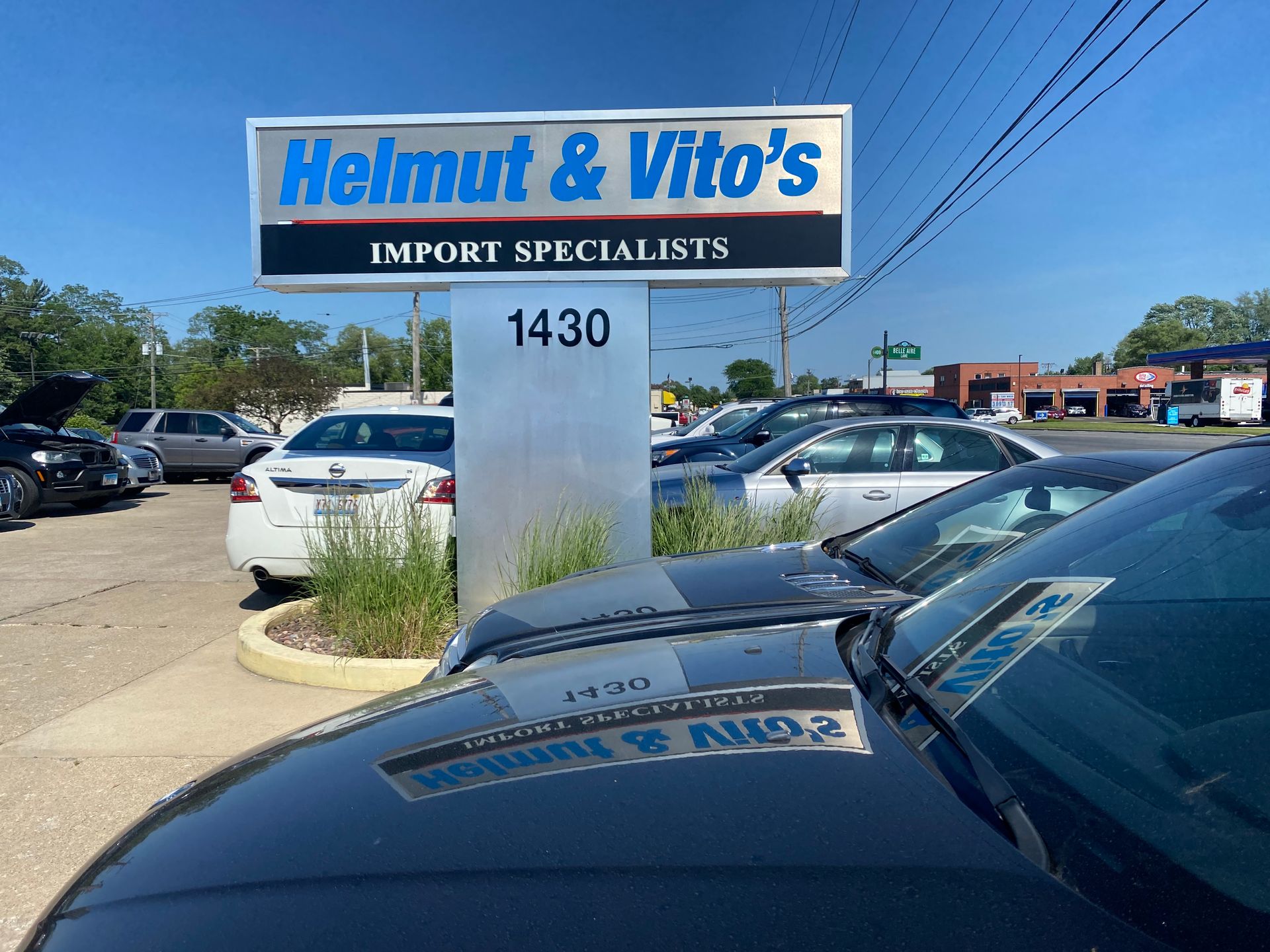 Helmut & Vito’s Import Specialists sign outside a car lot with parked vehicles and a police car in front