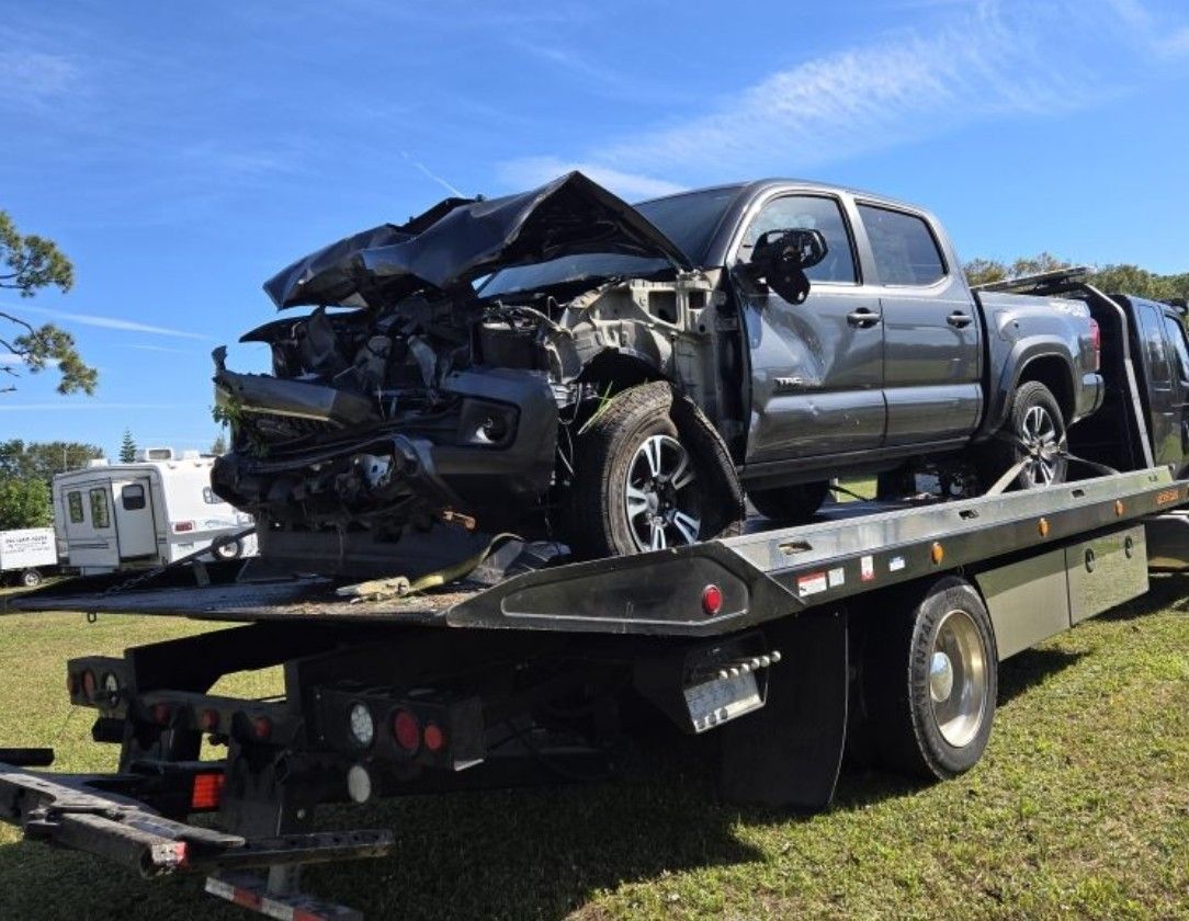 A crashed gray truck on the back of a black tow truck.