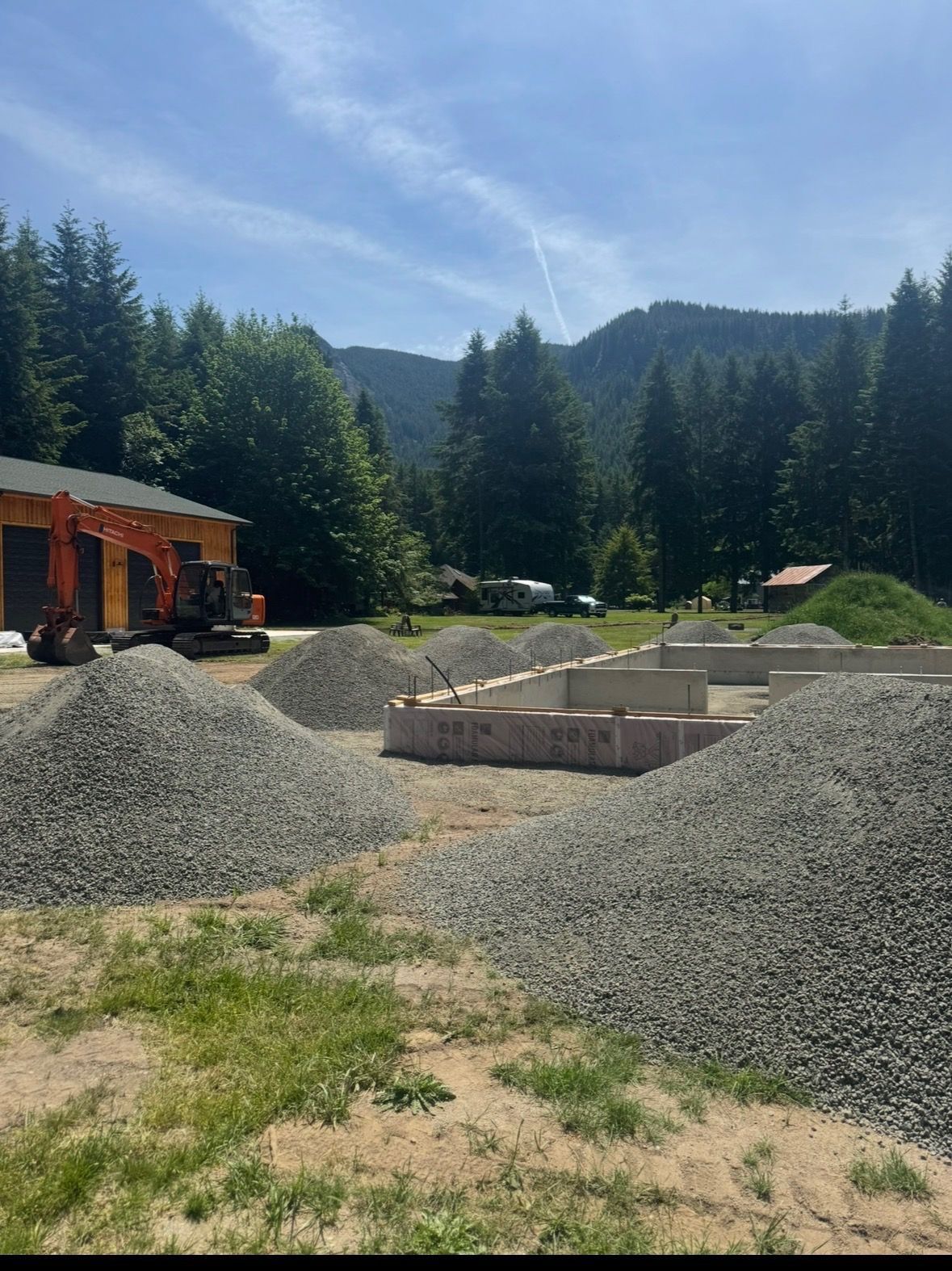 A black Kenworth dump truck parked on a gravel lot in front of a forest.