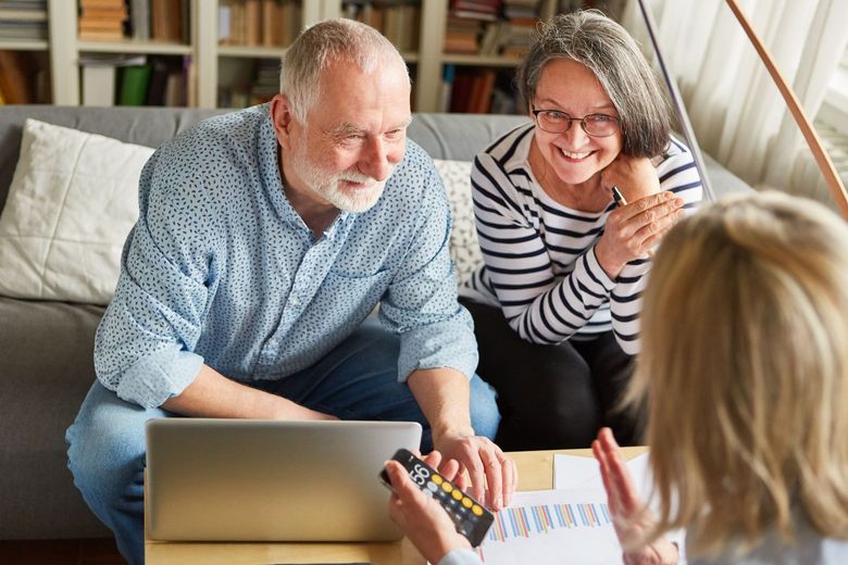 Couple consults with a financial advisor, looking at laptop and documents in a home setting.