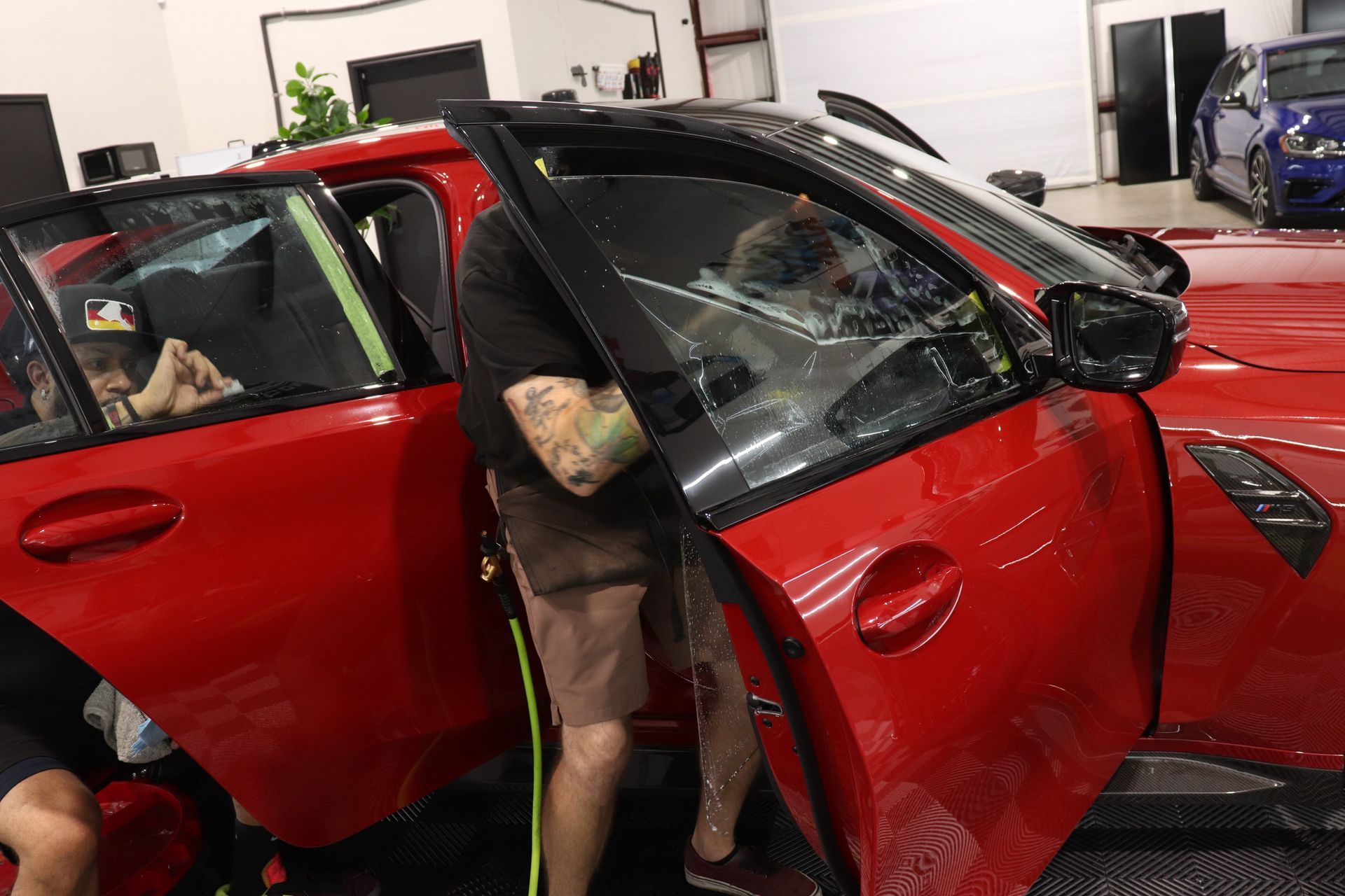 Red sports car with both doors open in a garage, showing the interior and a person leaning inside.
