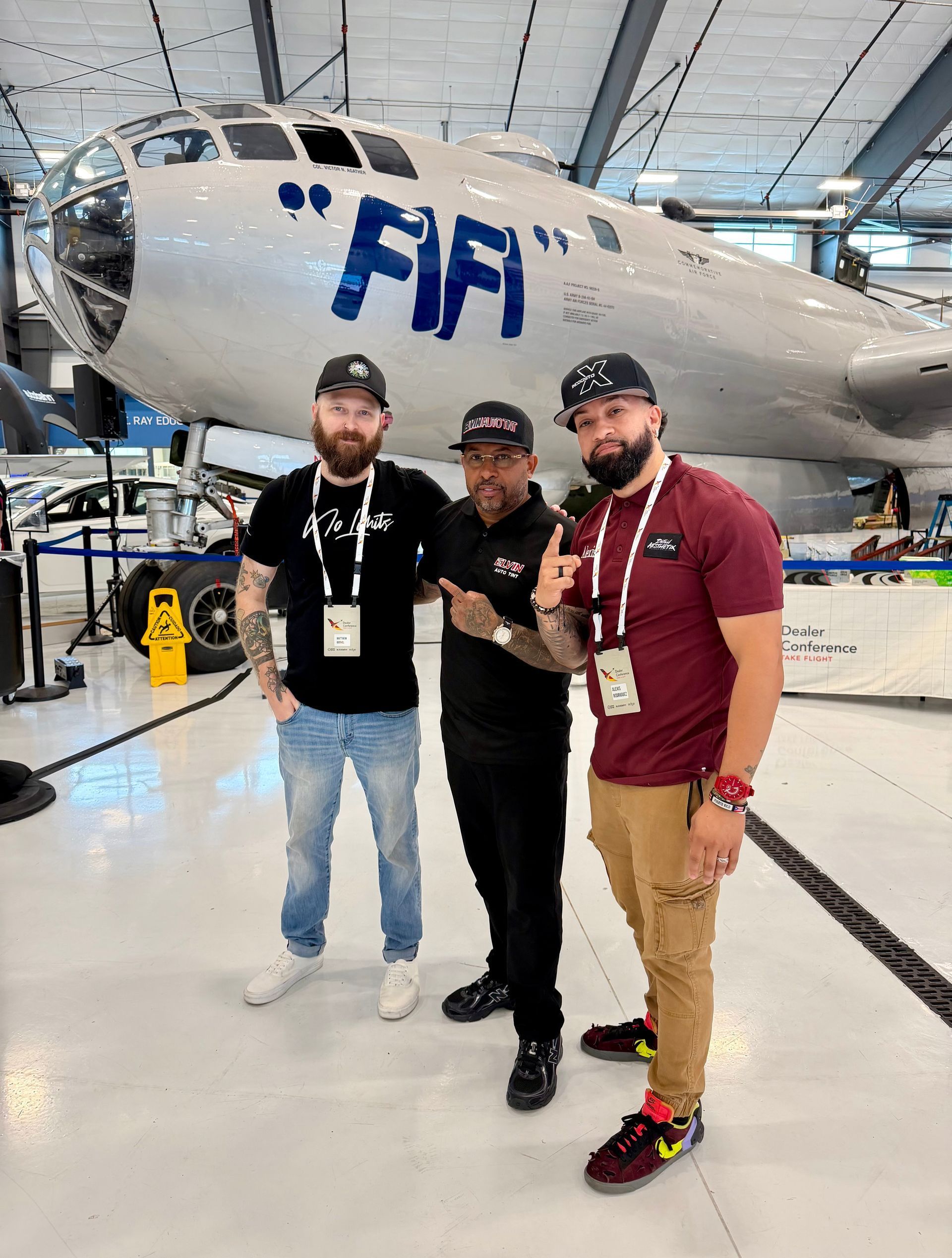 Three people posing in front of a silver FIA aircraft in a hangar.