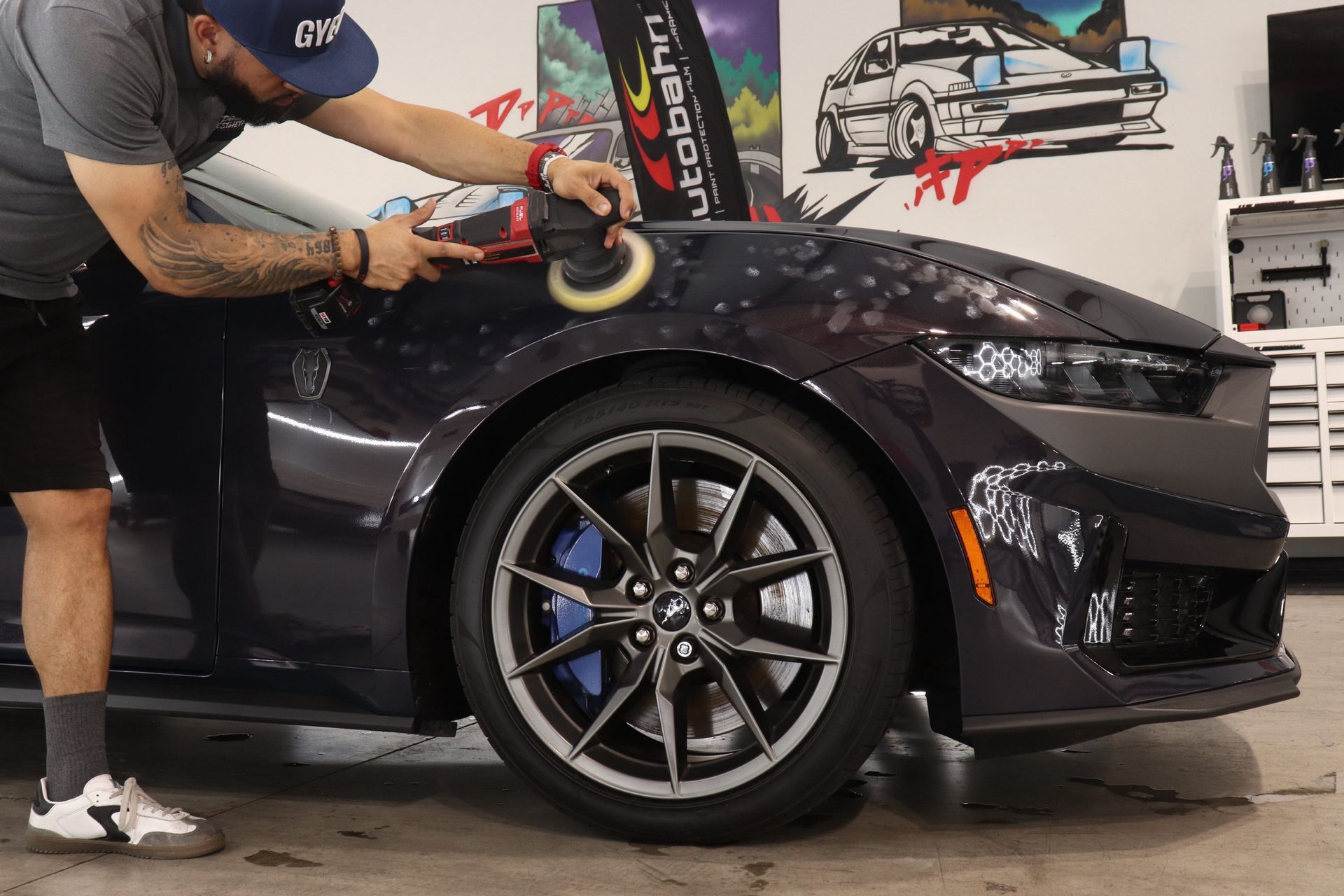 Detailing a black sports car with a person polishing the hood in a garage