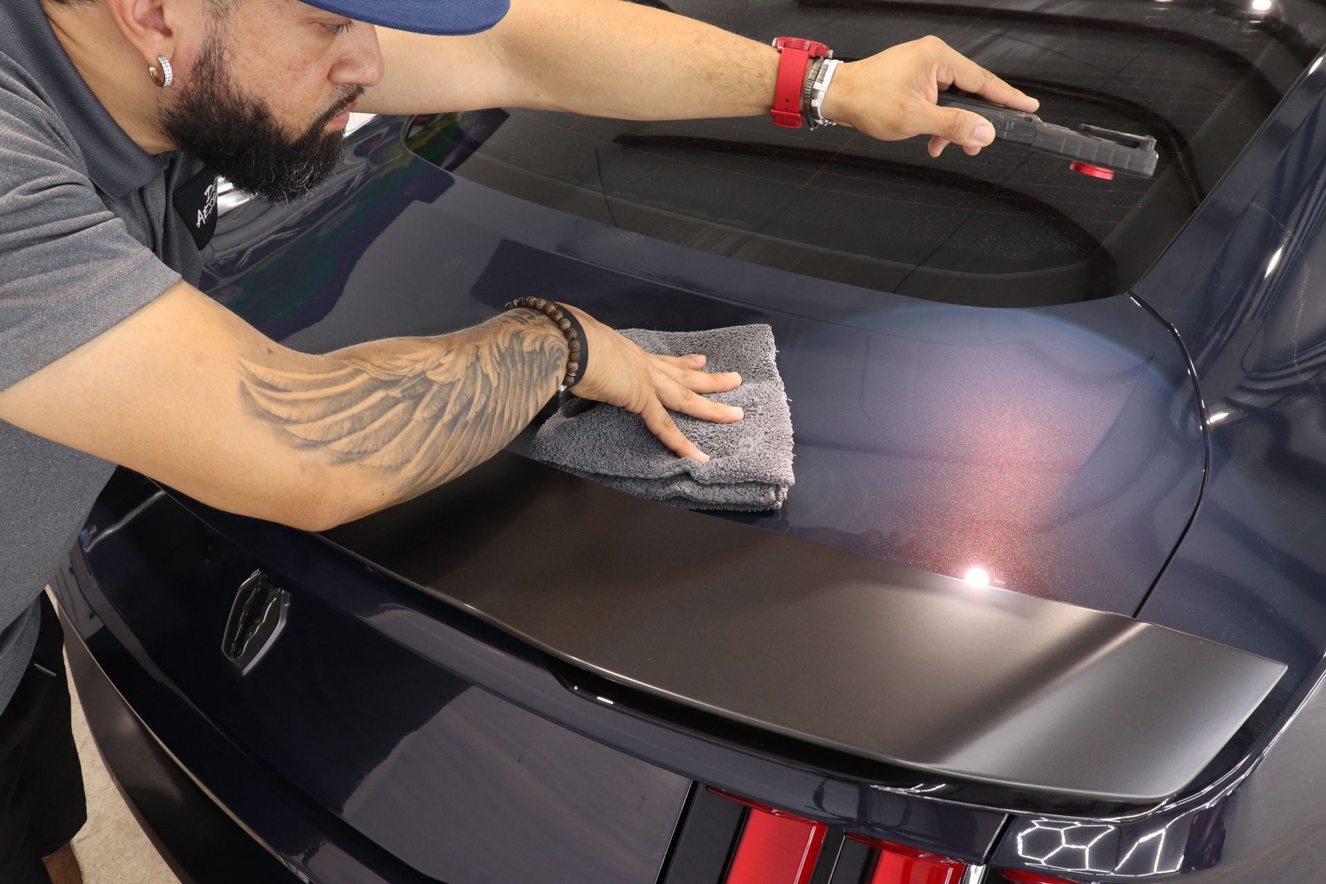 Person wiping a black car trunk with a cloth in a garage-like setting