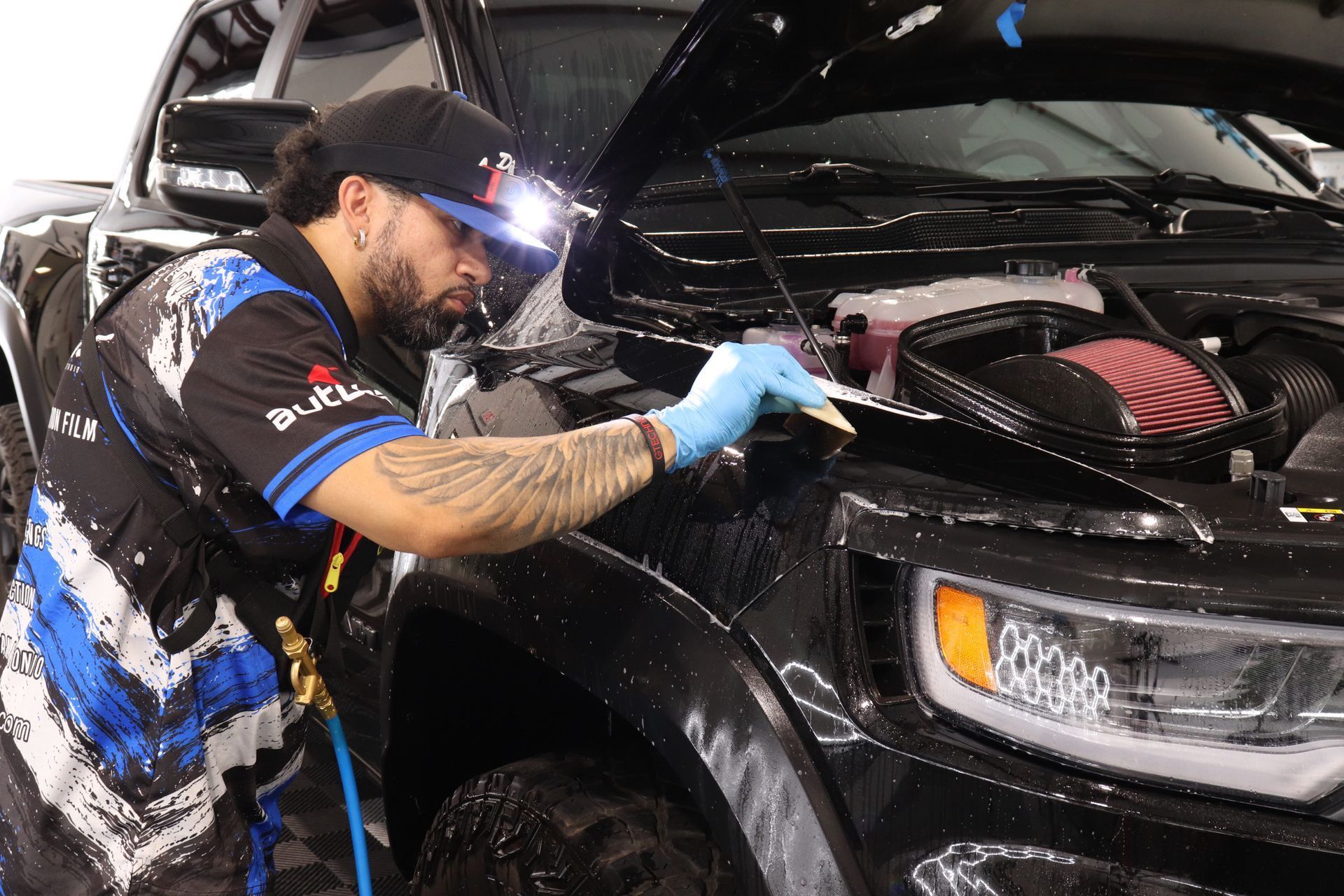 Black car being washed in a garage, covered in foam while a person scrubs the side.