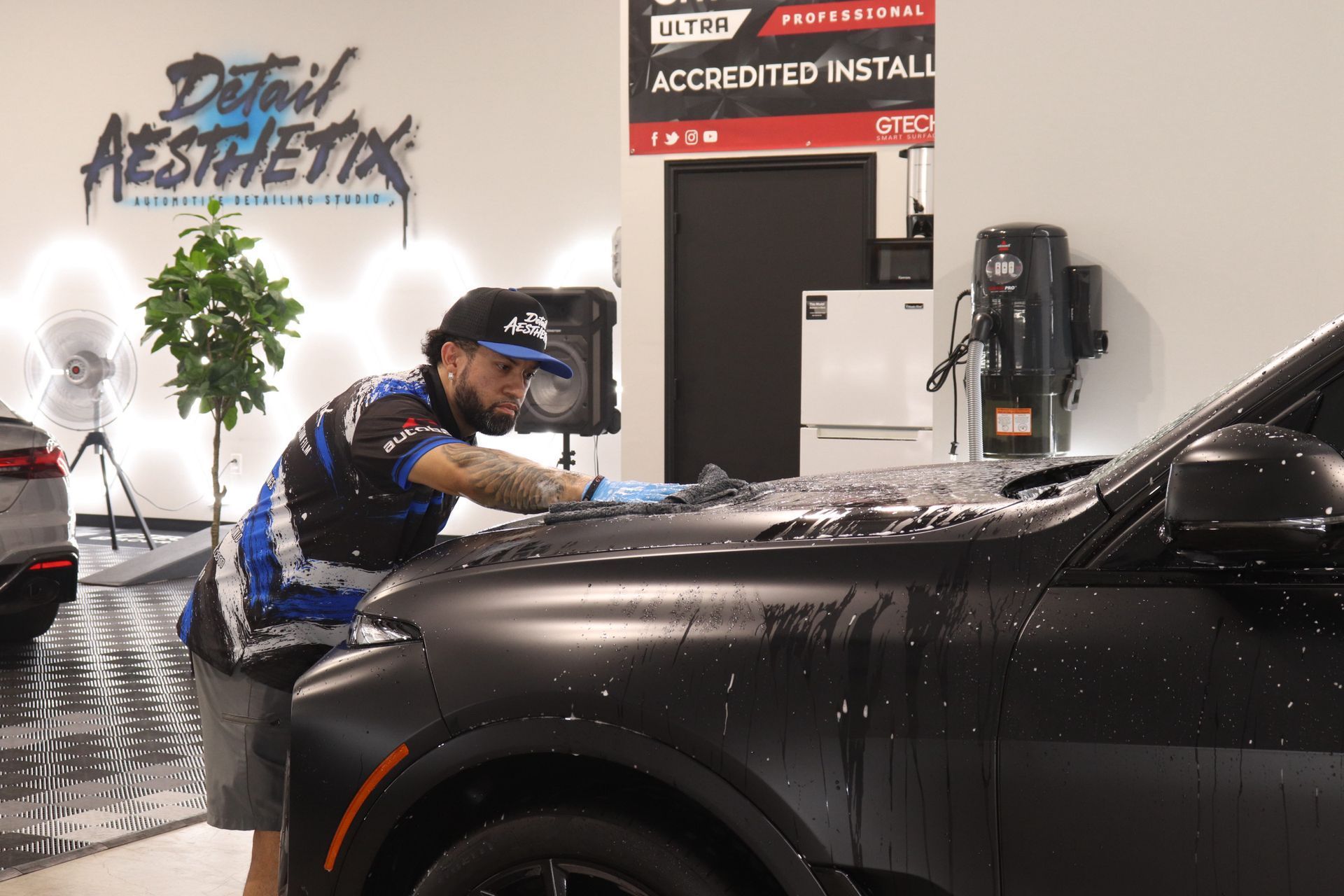 A person polishing the front fender of a black car with a blue cloth.