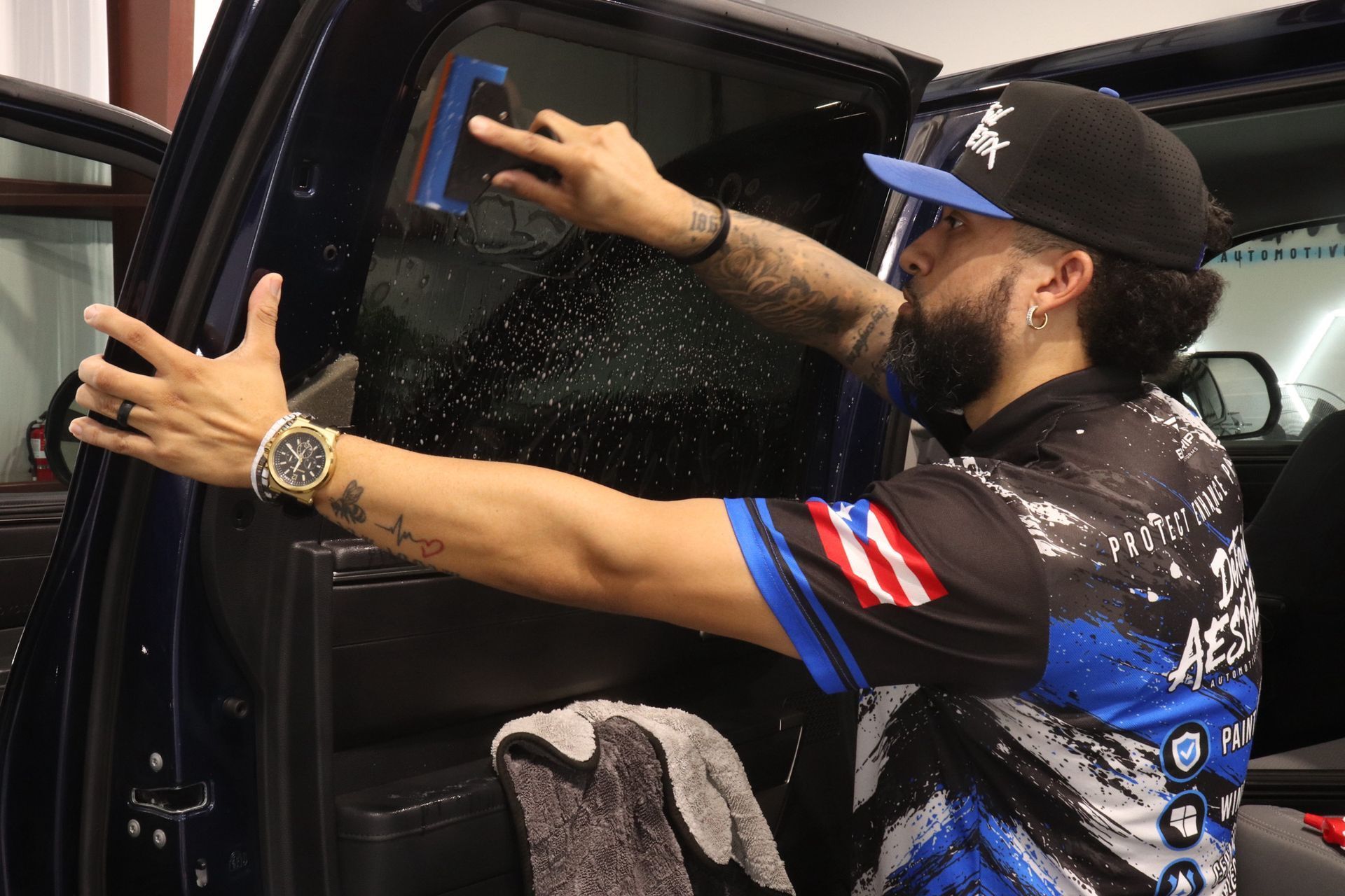 Person wiping a black car trunk with a cloth in a garage-like setting