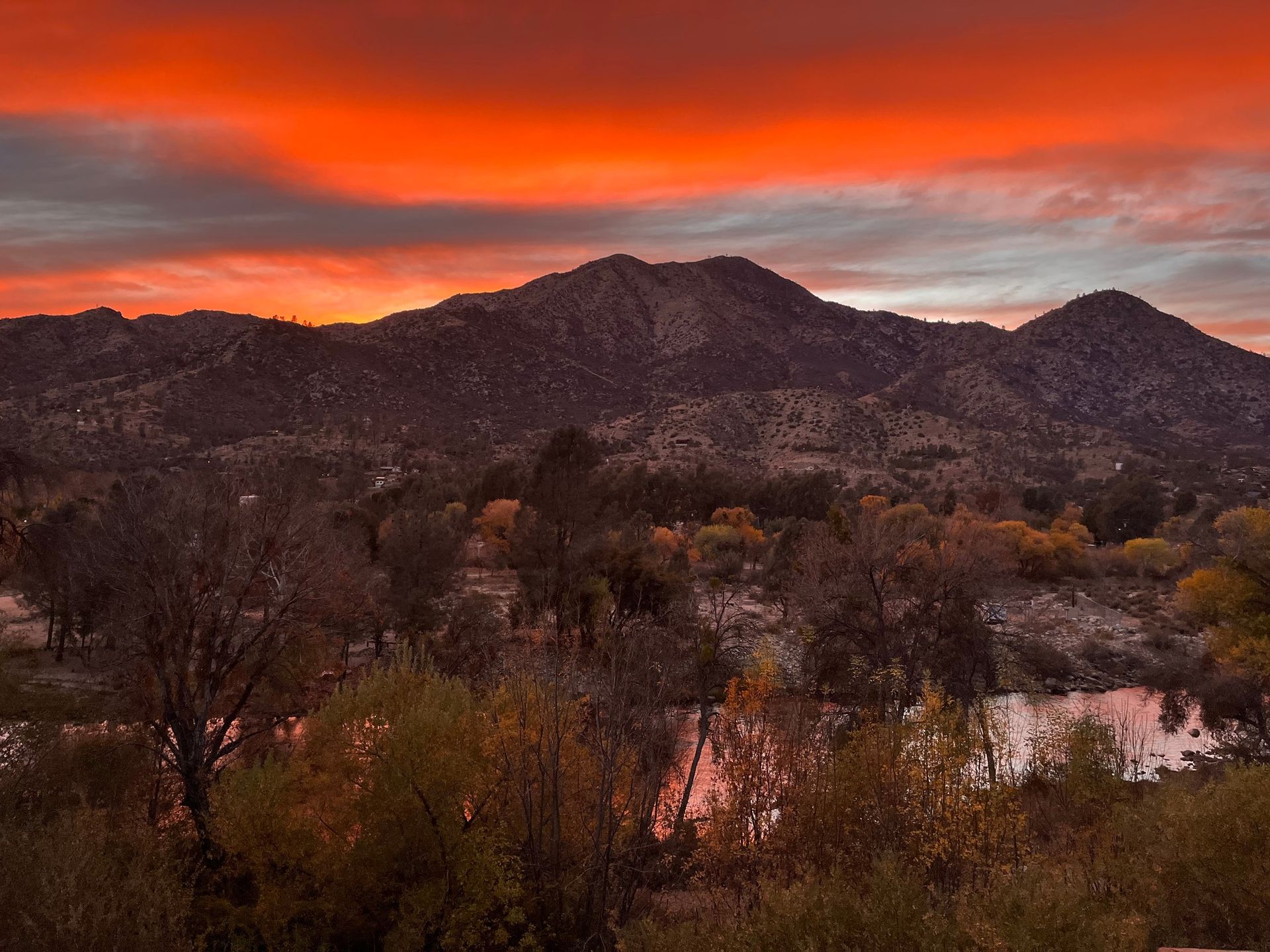 Fiery sunset over a mountain range and a river reflecting the orange sky.
