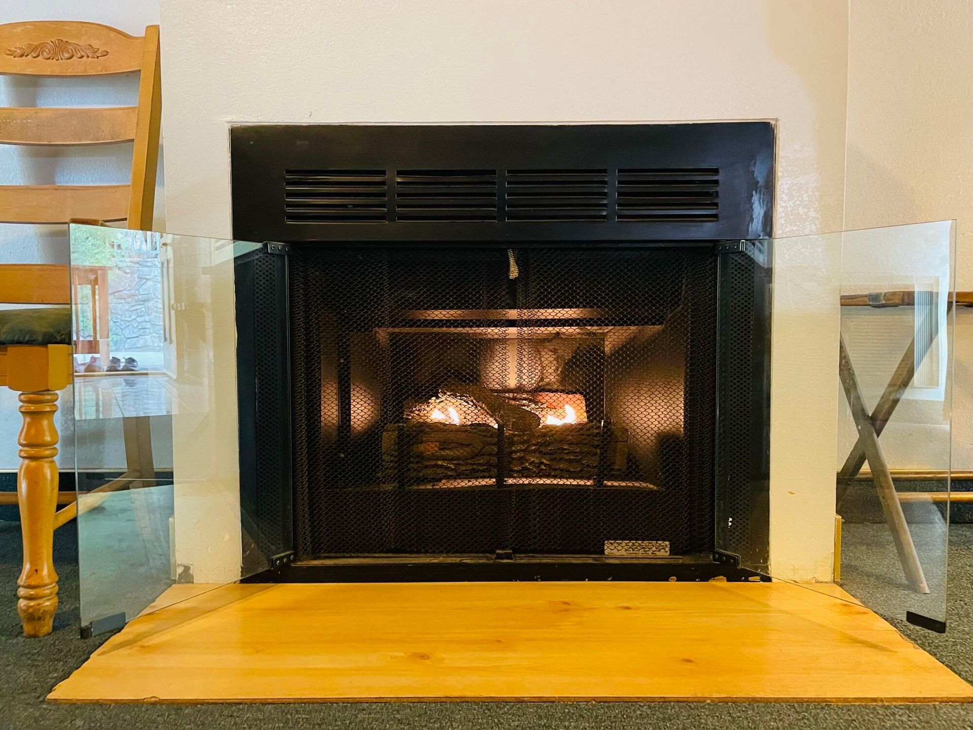 A fireplace with a burning fire, framed by a black metal grate and glass panels, set in a room.