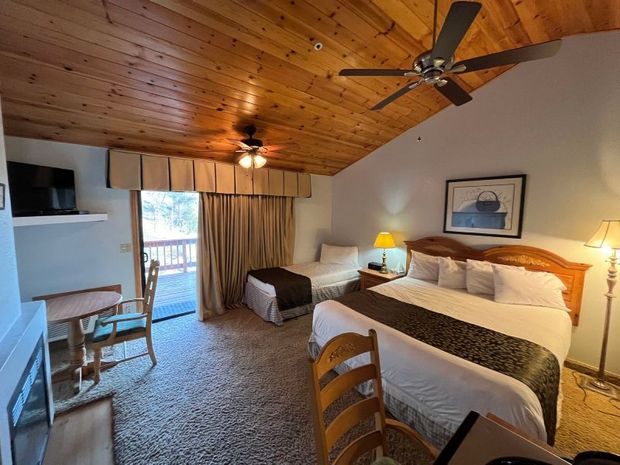 Hotel room with a bed, small sofa, table, and fireplace. Wooden ceiling and balcony access.