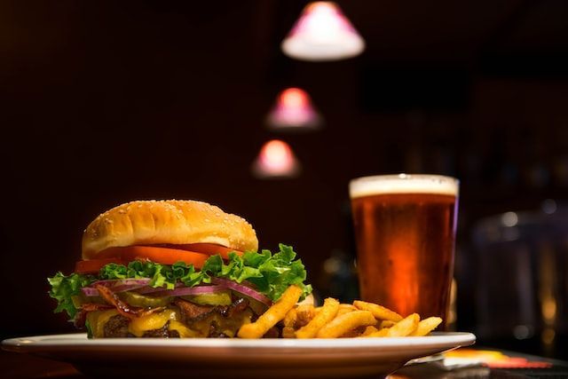 Burger with fries and beer on a plate, under dim lighting in a bar.