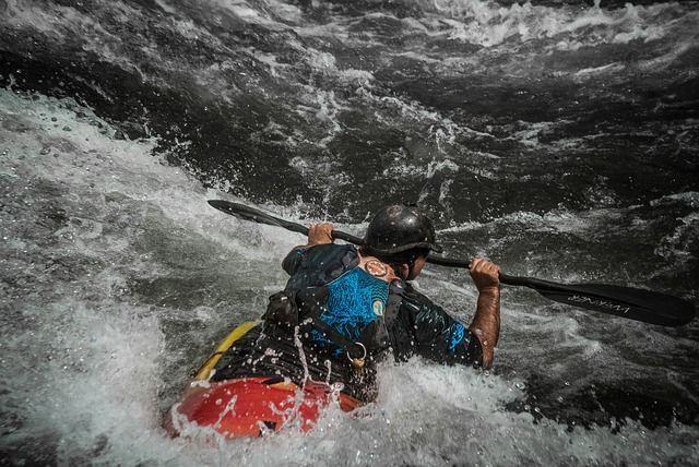 Kayaker paddles through whitewater rapids, wearing a helmet and life vest.