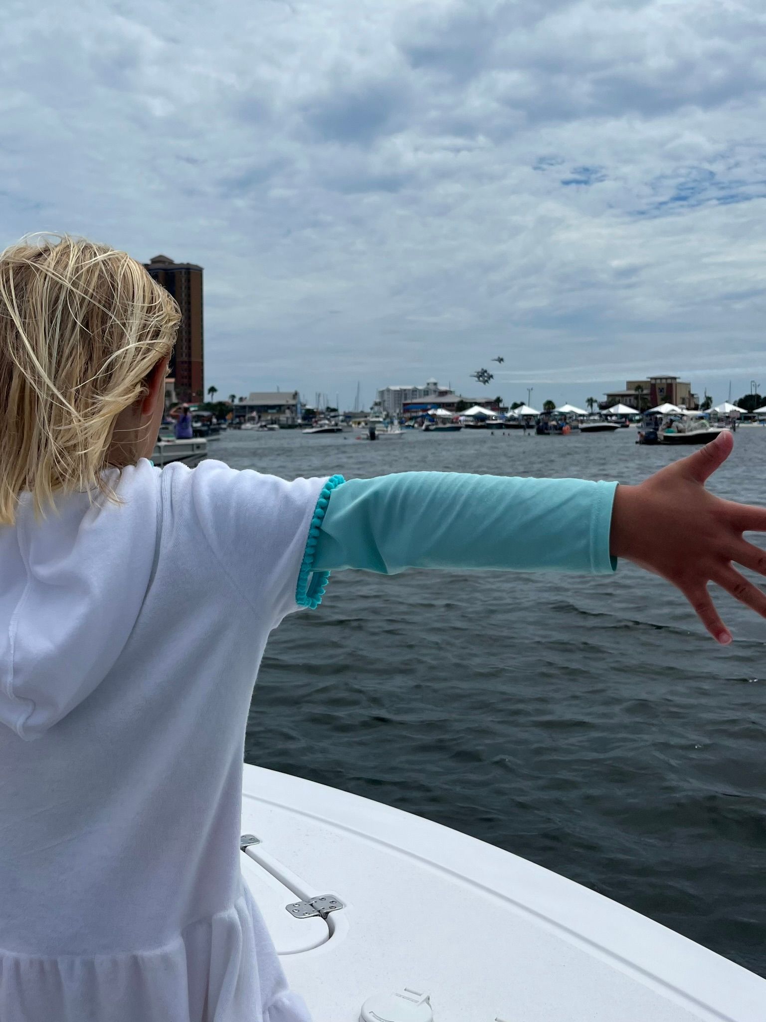 A little girl is standing on a boat with her arms outstretched.