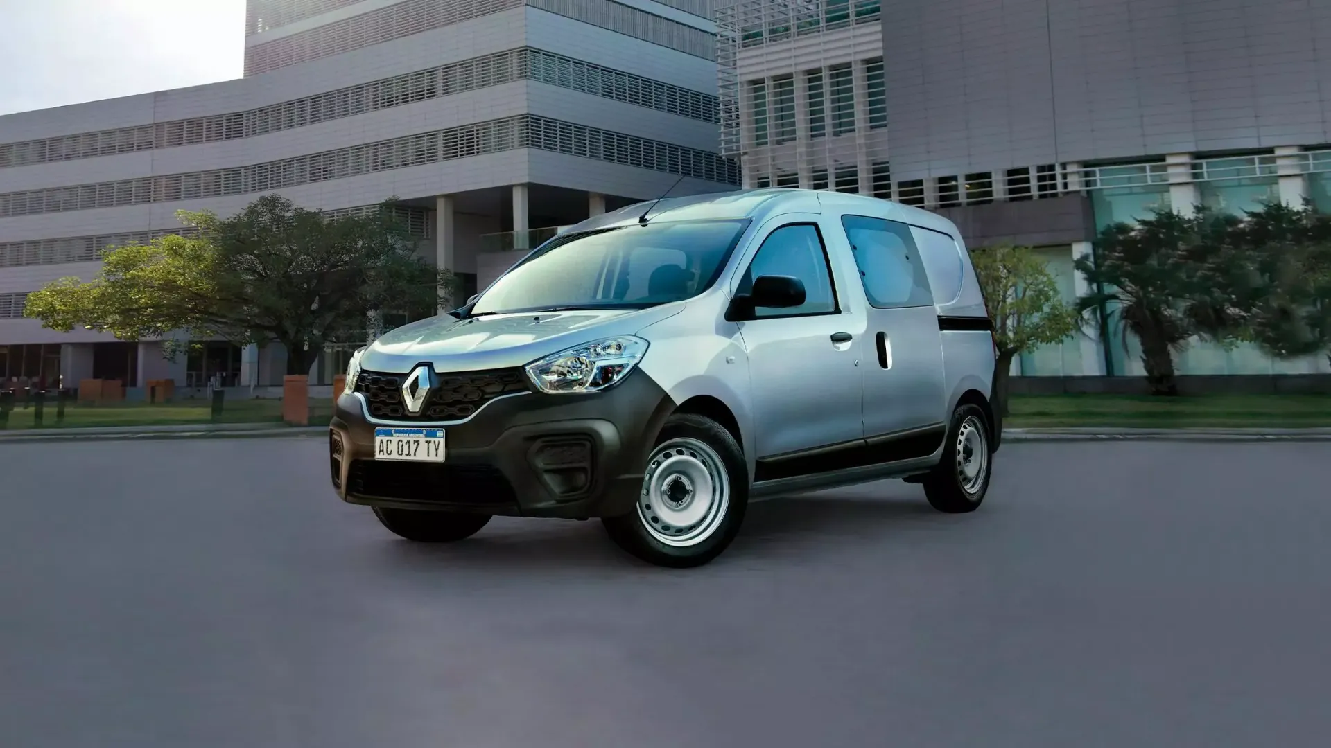 Furgoneta utilitaria Renault de color plata estacionada en una calle pavimentada frente a un edificio moderno.