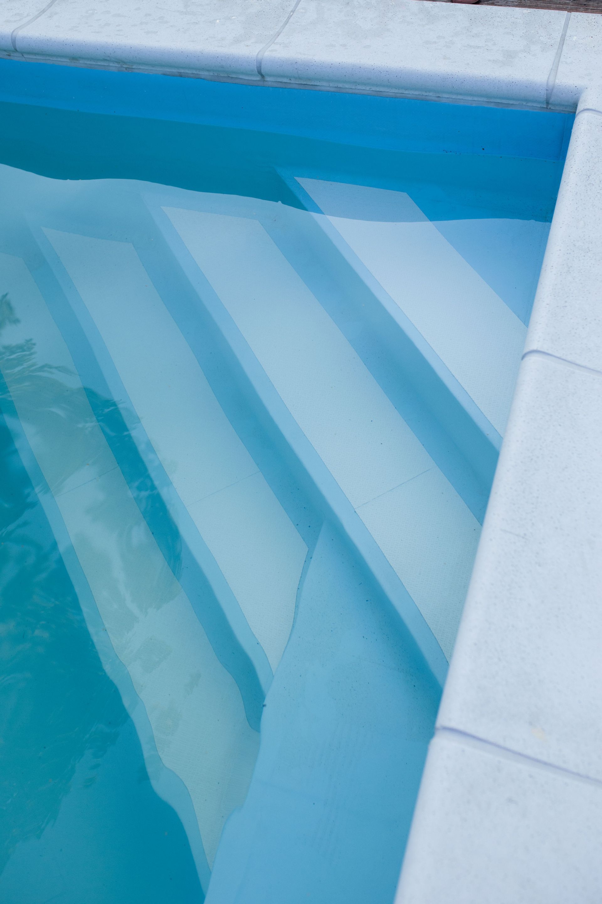 Escaleras de piscina con azulejos azules y ondas de agua, y borde blanco de la piscina.
