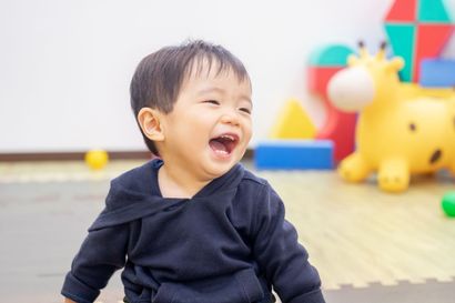 A baby is laughing in a play room with toys in the background.