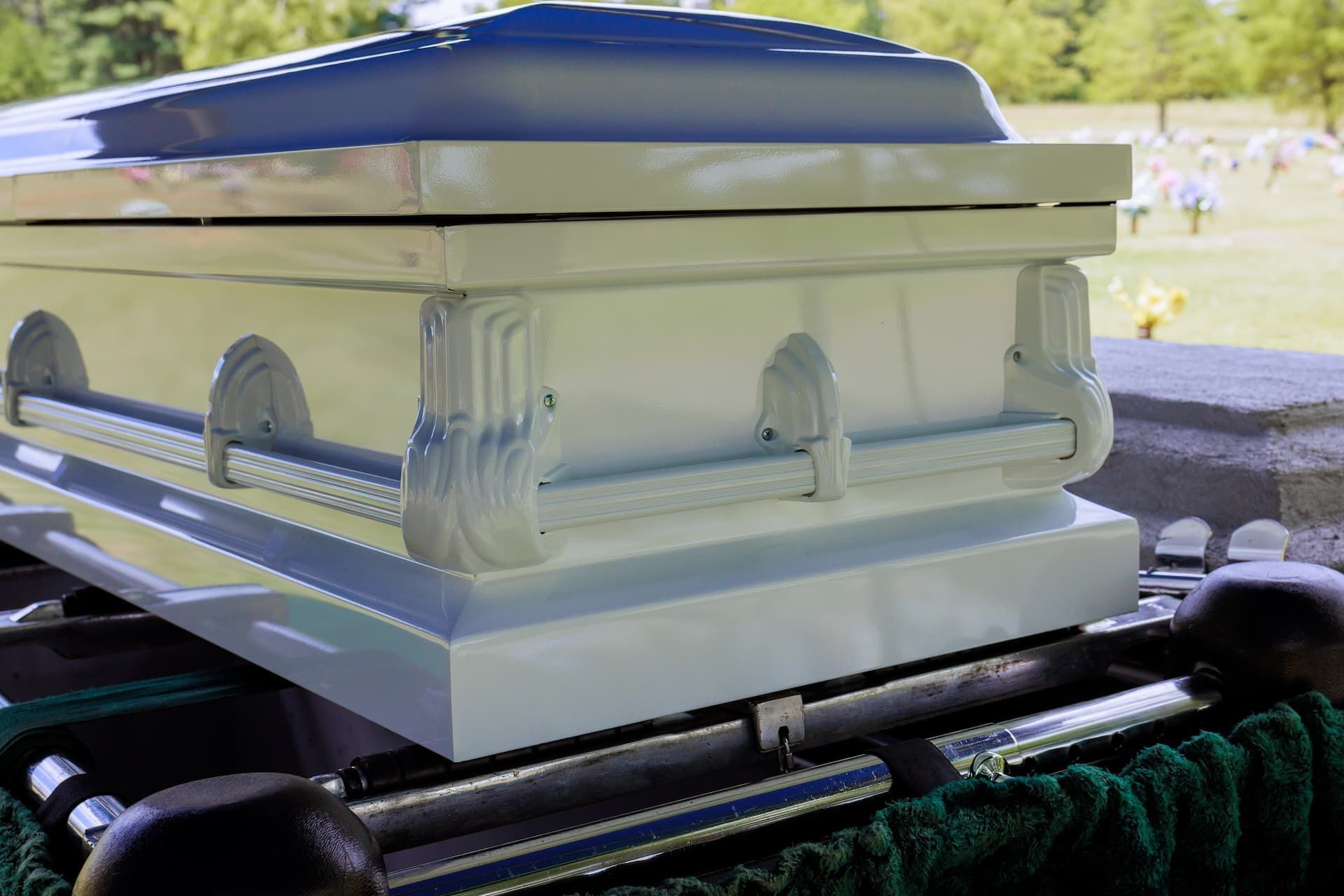 A closed wooden casket with candles, dried wheat, and flowers arranged on a draped surface.