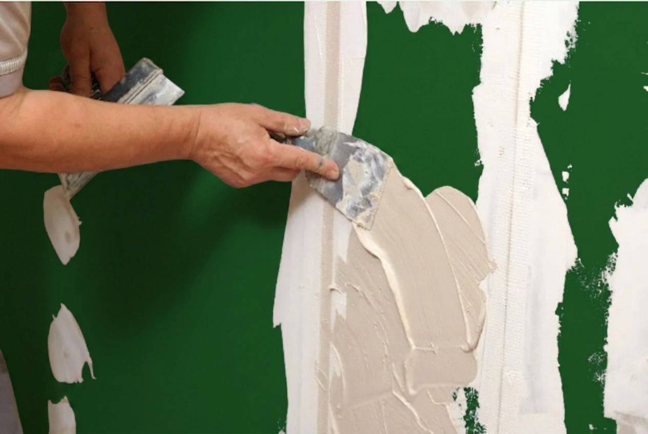 Person applying white plaster to a green wall with a putty knife
