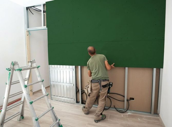 Worker installing large green wall panels in a room under renovation