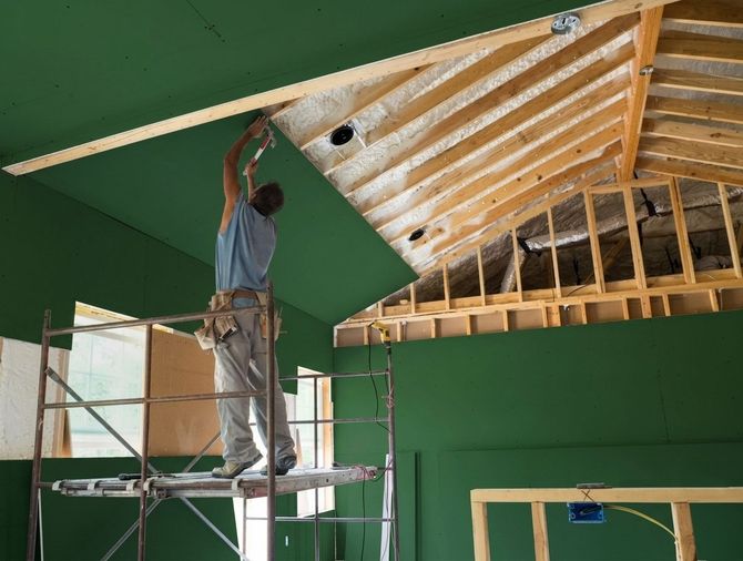 Worker on scaffolding installing ceiling boards in a green-walled room