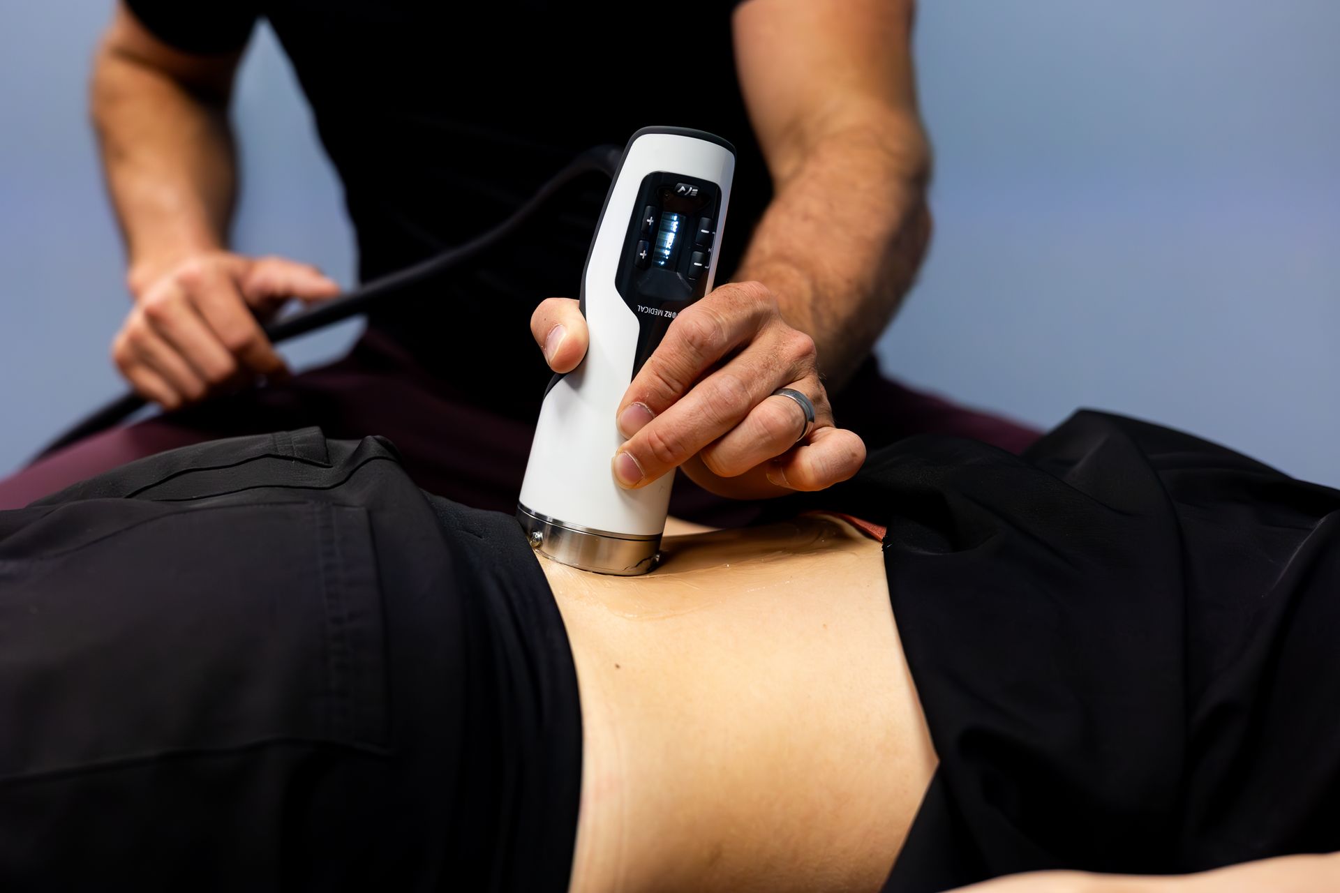 Therapist using a white ultrasound device on a patient's lower back.