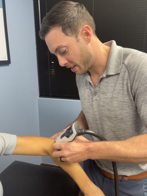 A man in a grey shirt is examining a patient 's arm