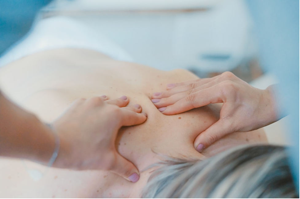 Hands giving a shoulder massage to a person lying face down on a massage table.