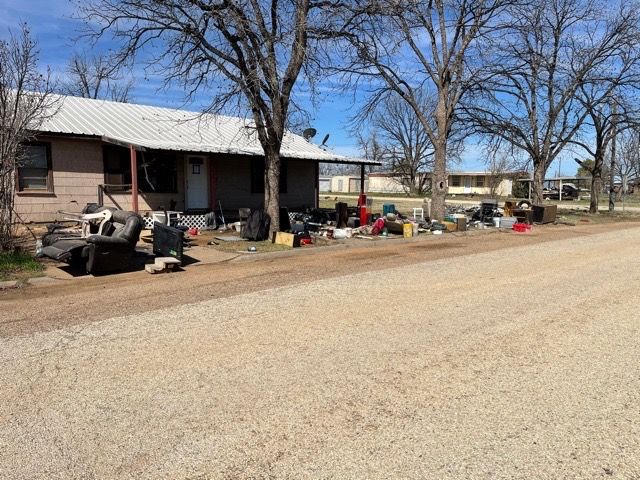 A house exterior with a large amount of clutter and discarded items scattered across the front yard and porch.