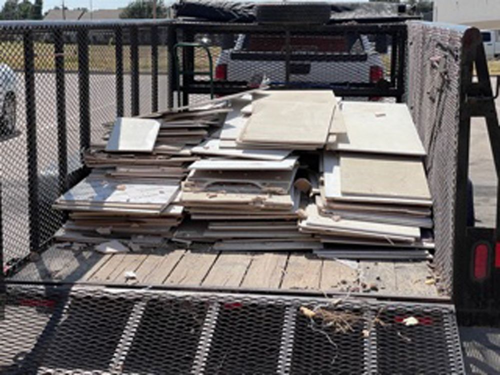 A utility trailer filled with stacks of light-colored, flat construction debris or wood panels.