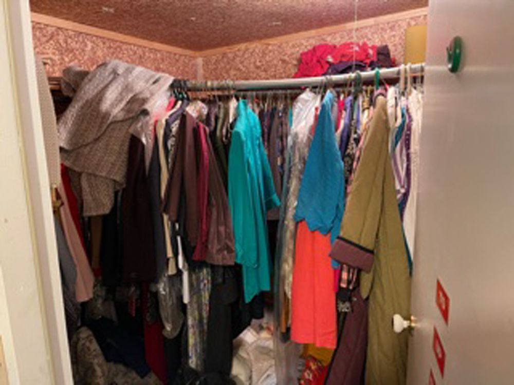 A cluttered closet filled with various hanging clothes on a curved rack against patterned wallpaper.