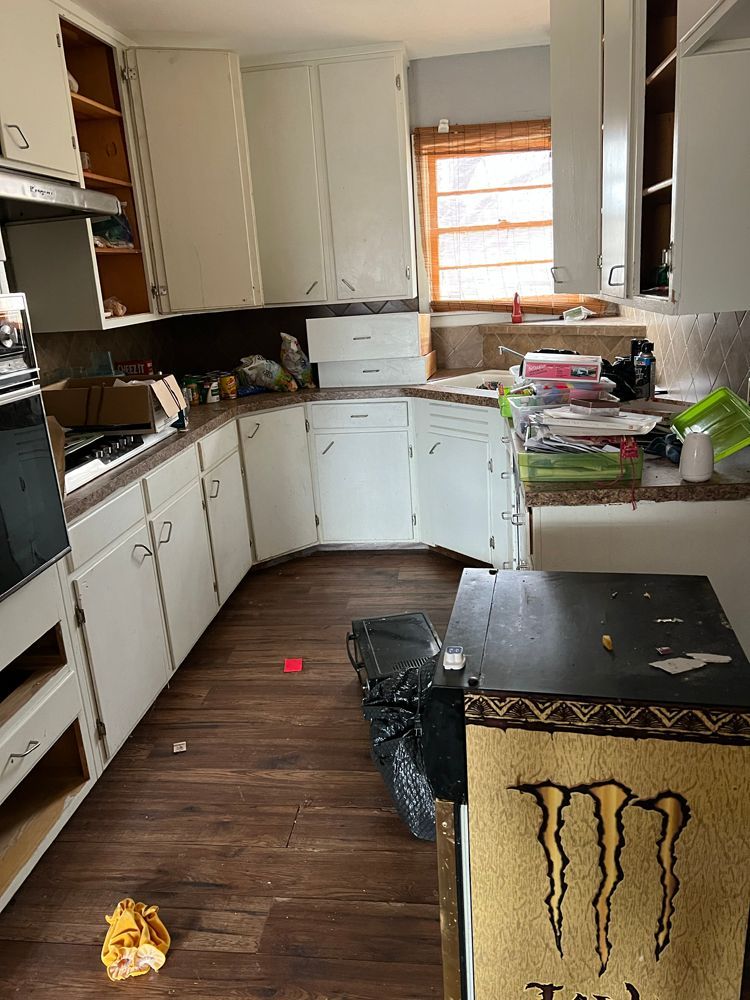 A cluttered kitchen with white cabinets, wood-look flooring, and a black Monster Energy branded item in the foreground.