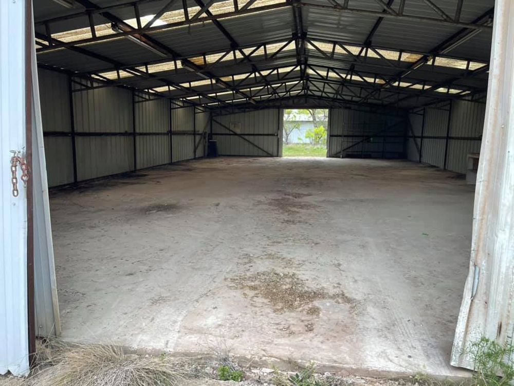 Interior view of a large, empty metal warehouse with a concrete floor and a wide-open rear doorway.