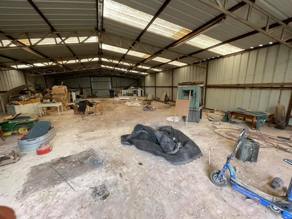 An interior view of a large, cluttered metal shed with natural light shining through translucent roof panels.