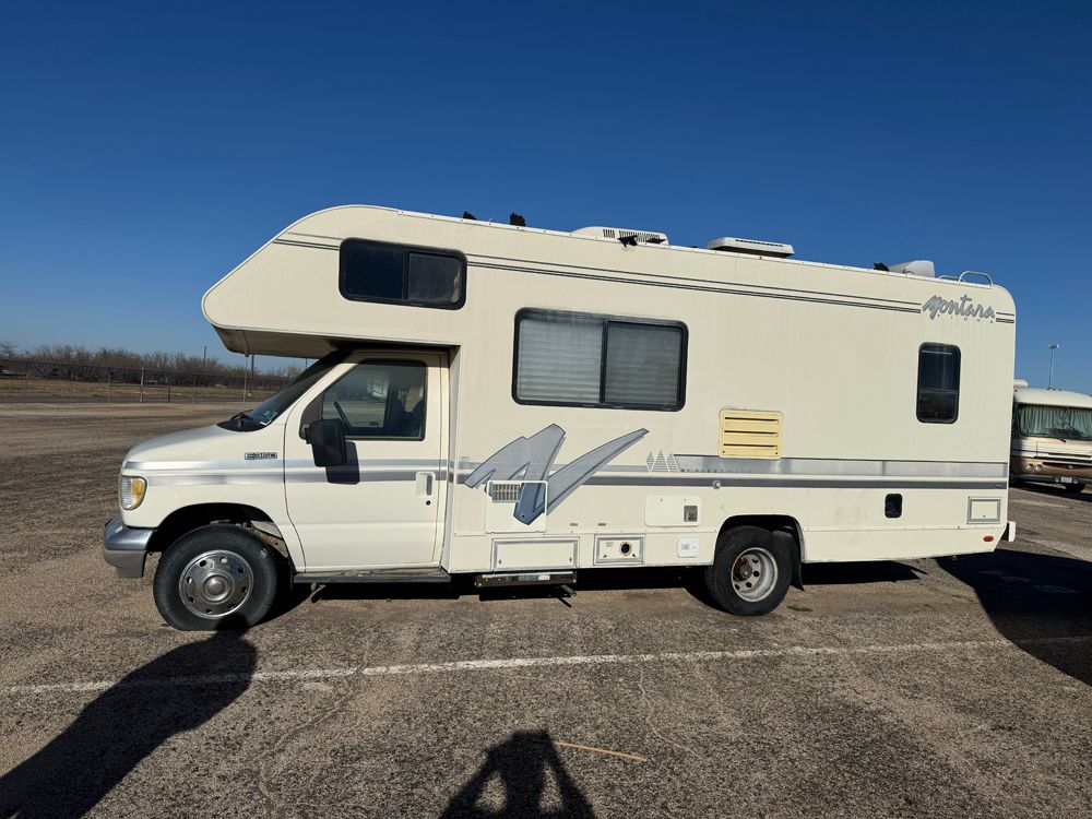 A white Class C motorhome parked on an asphalt lot under a clear blue sky.