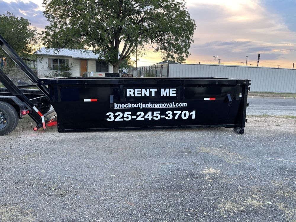 A black roll-off dumpster trailer parked on a gravel lot, featuring the text "RENT ME", a website, and phone number.