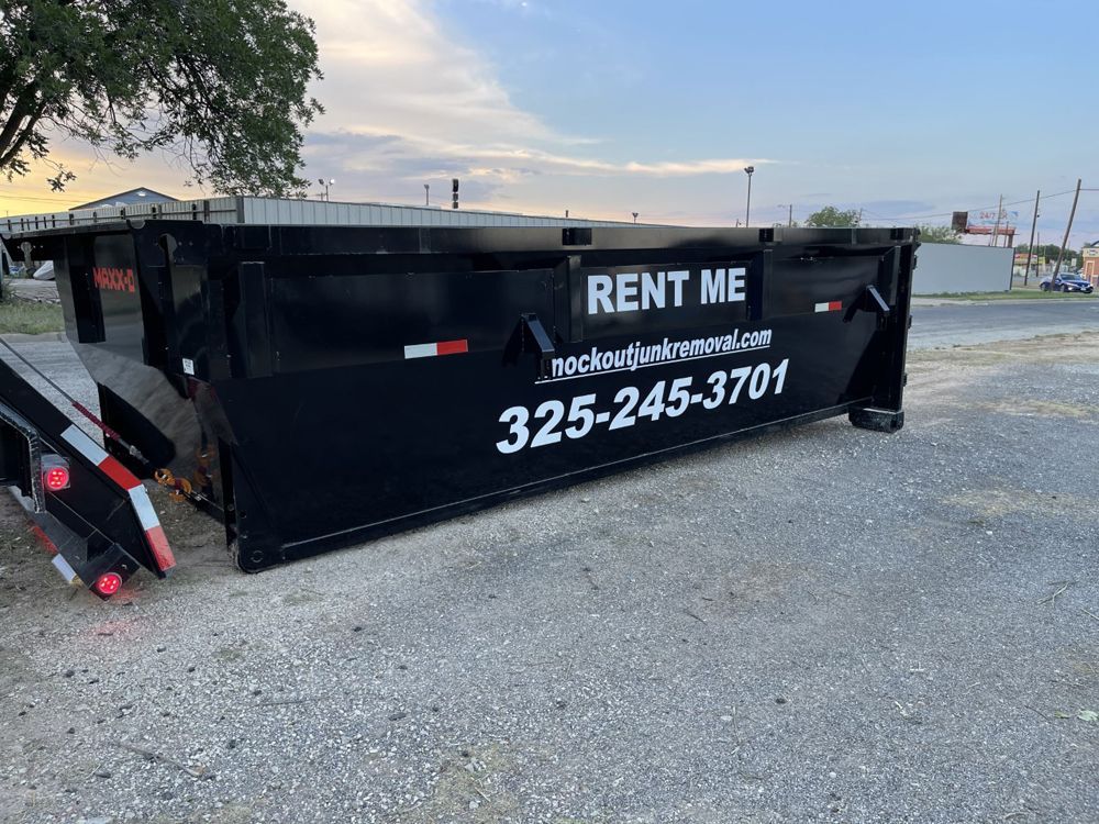 A black roll-off dumpster parked on a gravel lot, featuring the text "RENT ME" and a phone number on its side.