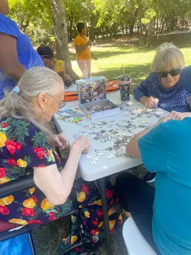 People working on a jigsaw puzzle at an outdoor table; sunny day.