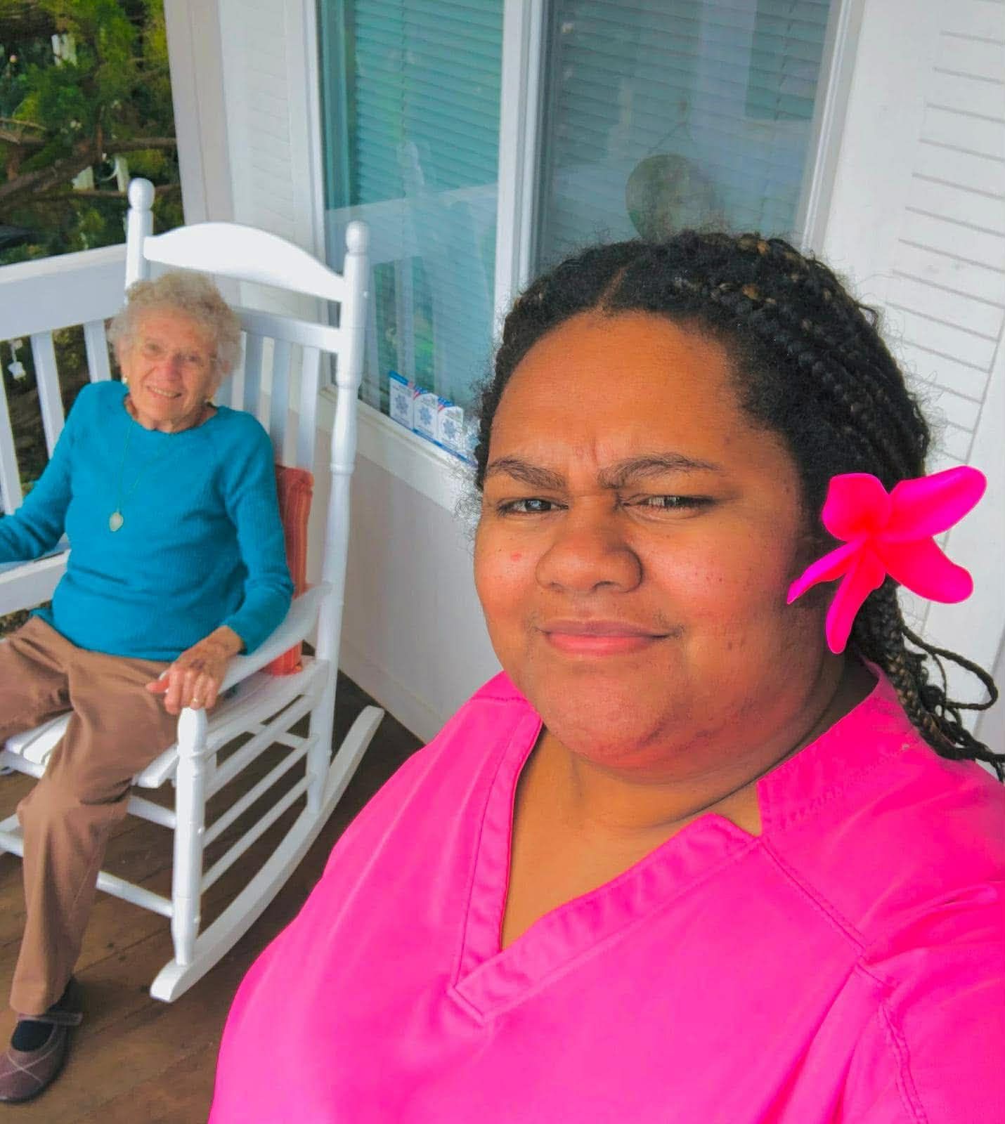 Woman in blue shirt cleans table with spray bottle; older woman sits in living room.