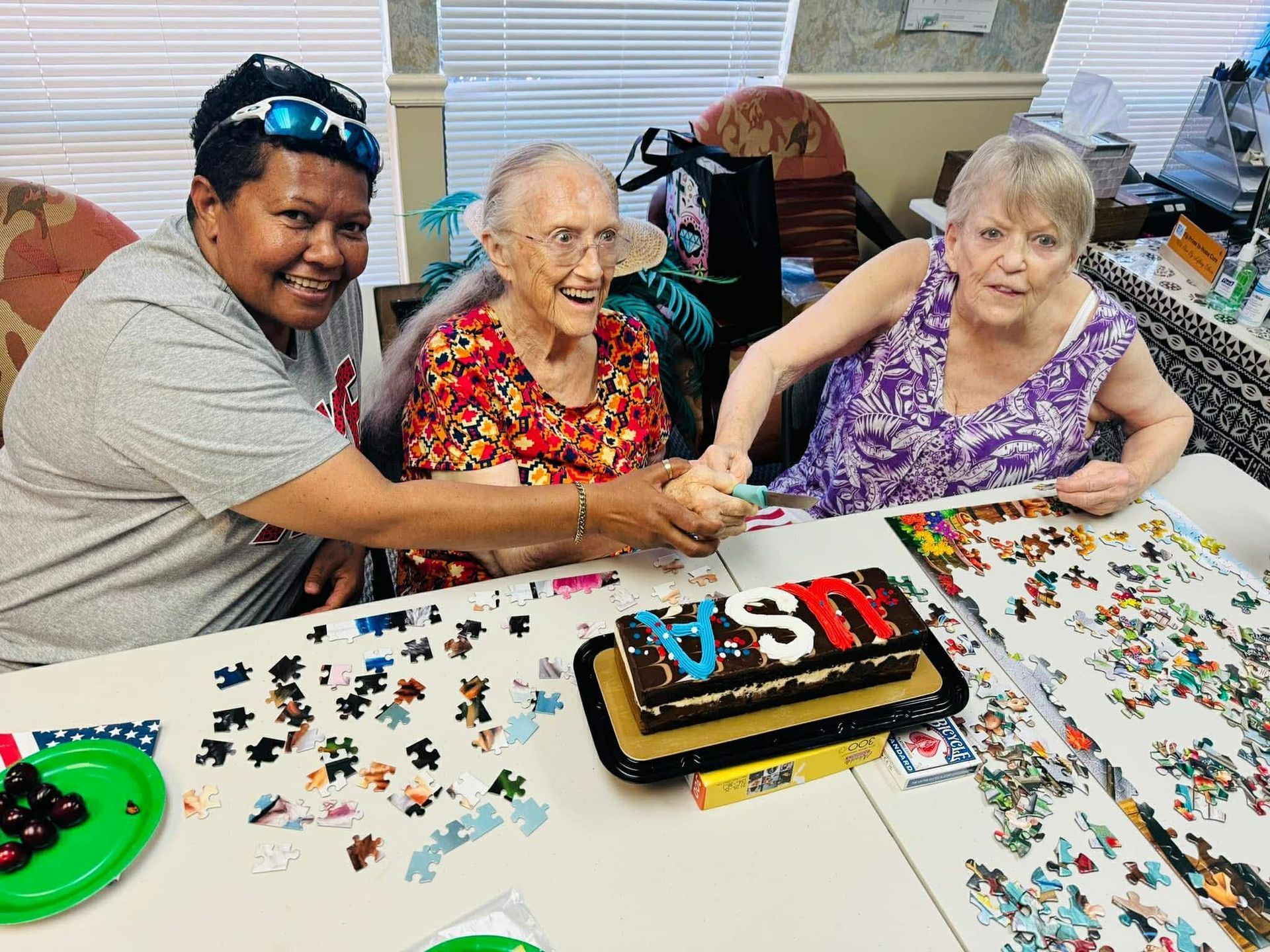 Three people at a table; they are working on a puzzle and there is a cake that says