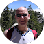 Bald man wearing sunglasses smiles broadly outdoors, possibly a mountainous setting.