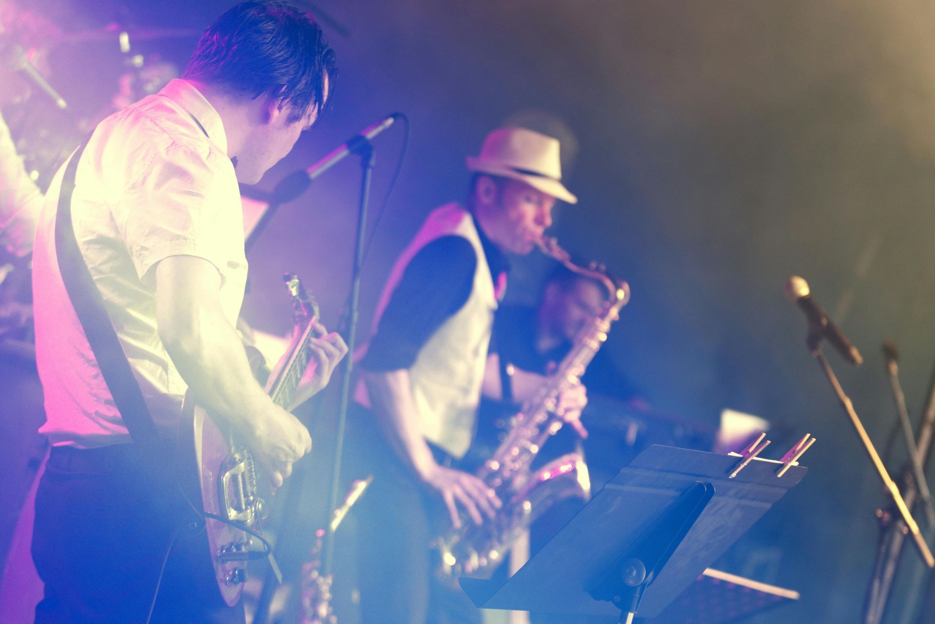 Banda tocando en vivo en el escenario, con el saxofonista en foco y luces de escenario azules y rosas.