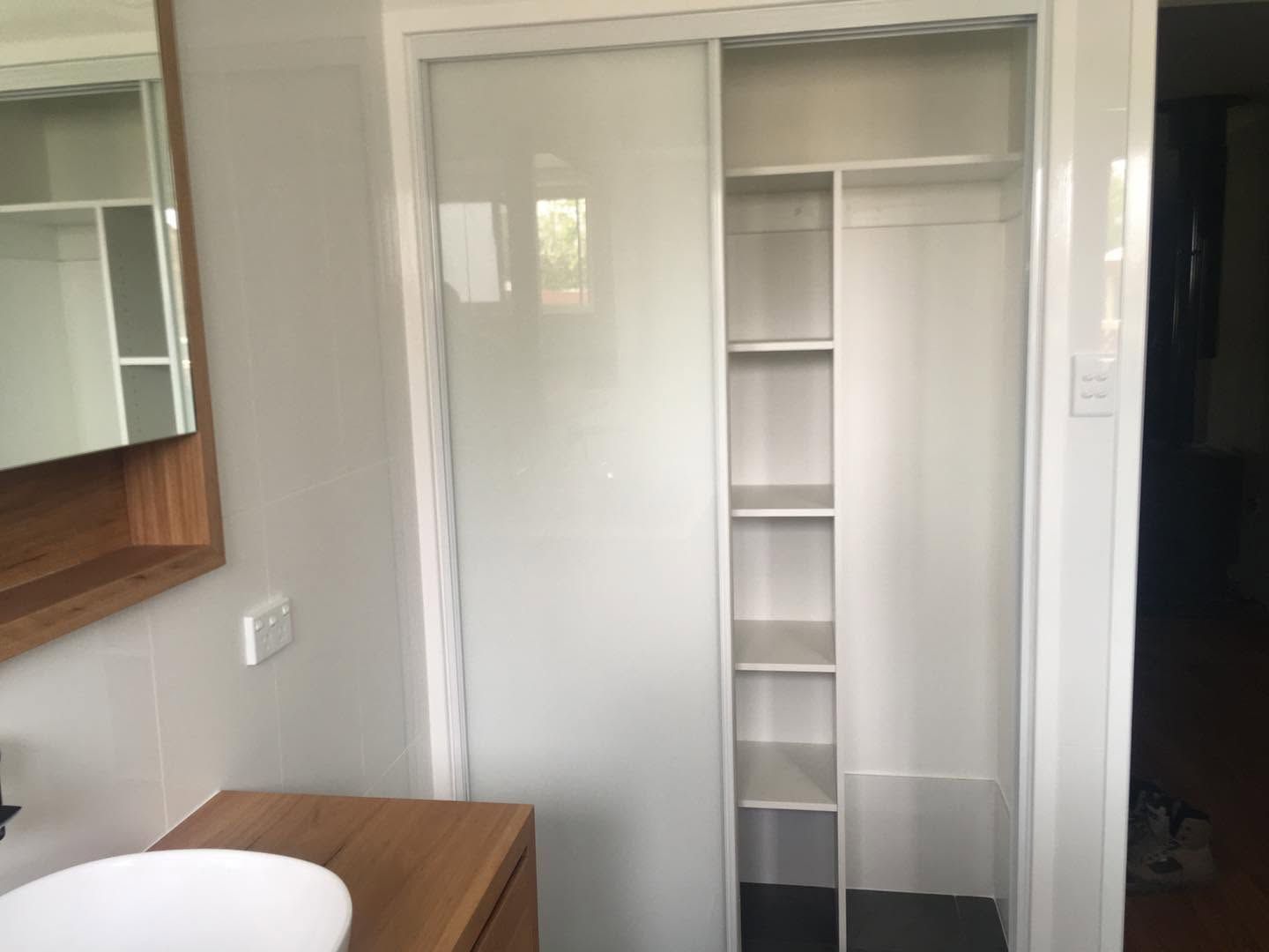 Small closet with sliding white doors and built-in shelves in a light gray room.