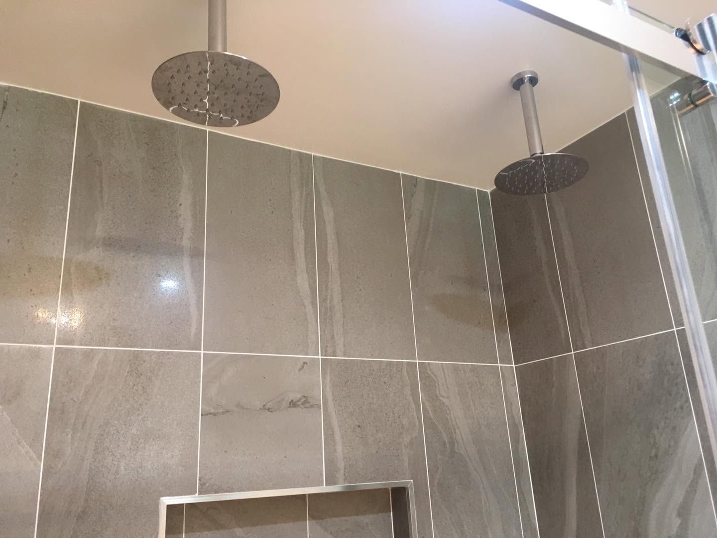 Glass shower enclosure with gray tiled walls and two round shower heads.