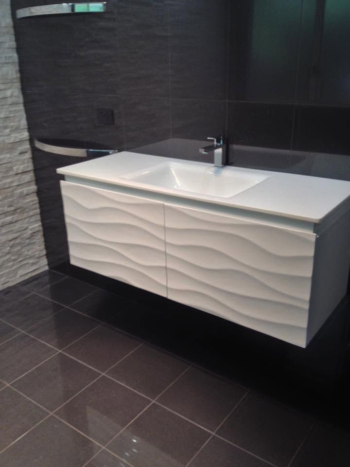 Modern white vanity with sink and wavy front panel in a dark tiled bathroom