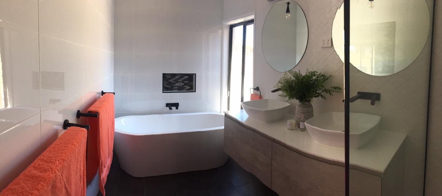 Modern bathroom with a white soaking tub, glass shower, red towel, round mirrors, and a plant on the vanity.