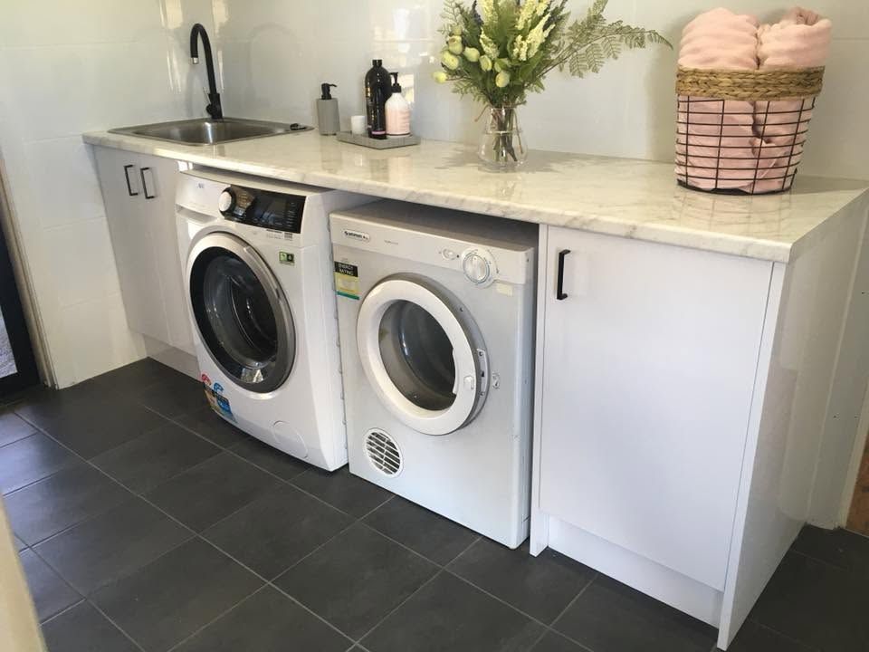 Laundry room with two white front-loading machines under a countertop and sink, plus cabinets and decor.