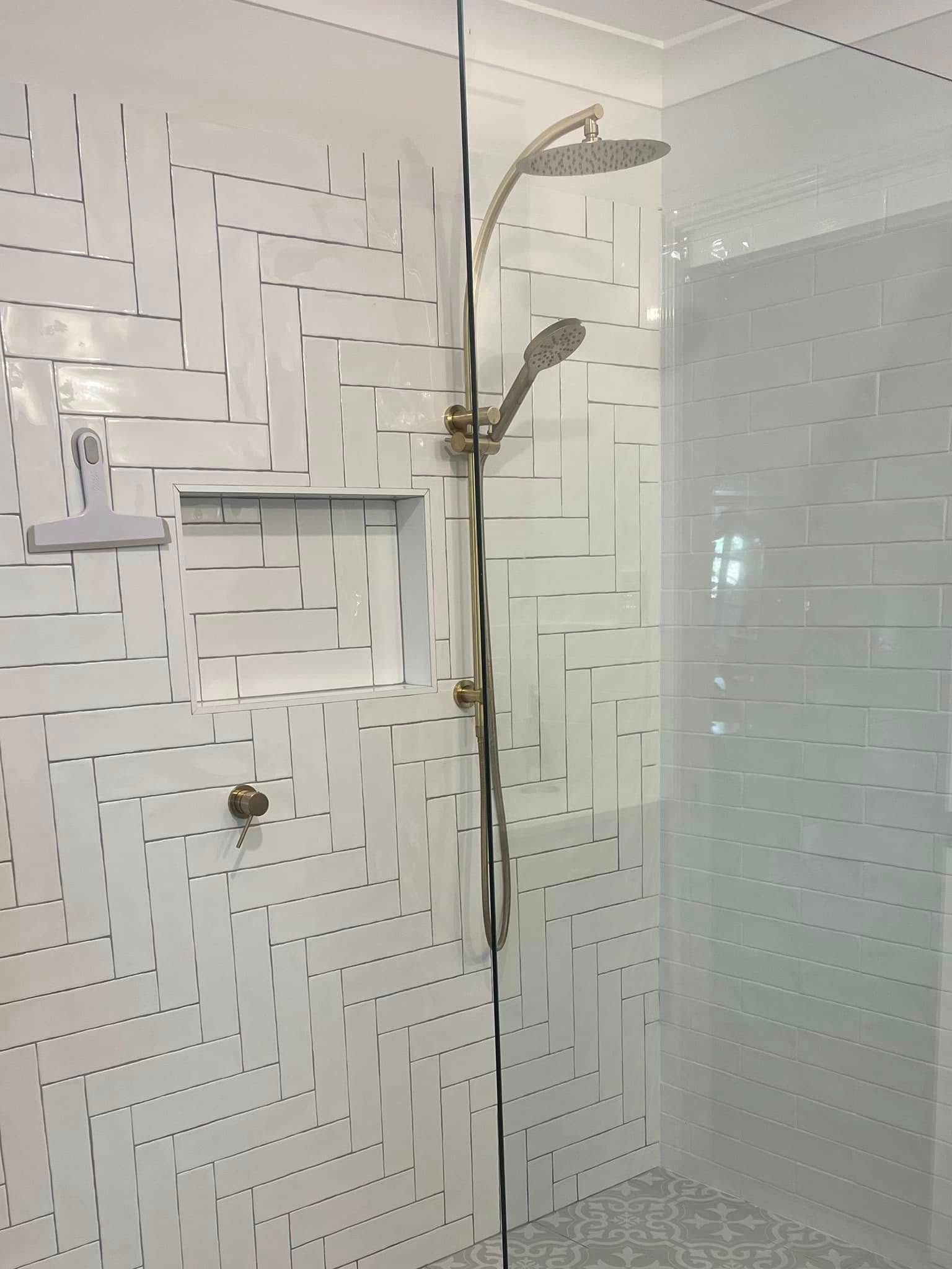 Modern bathroom shower with white tiled walls, glass partition, and chrome handheld showerhead.