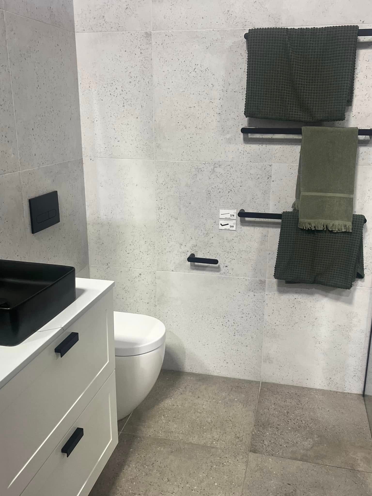 Modern bathroom with toilet, vanity, and wall-mounted towels on a light gray tiled wall.